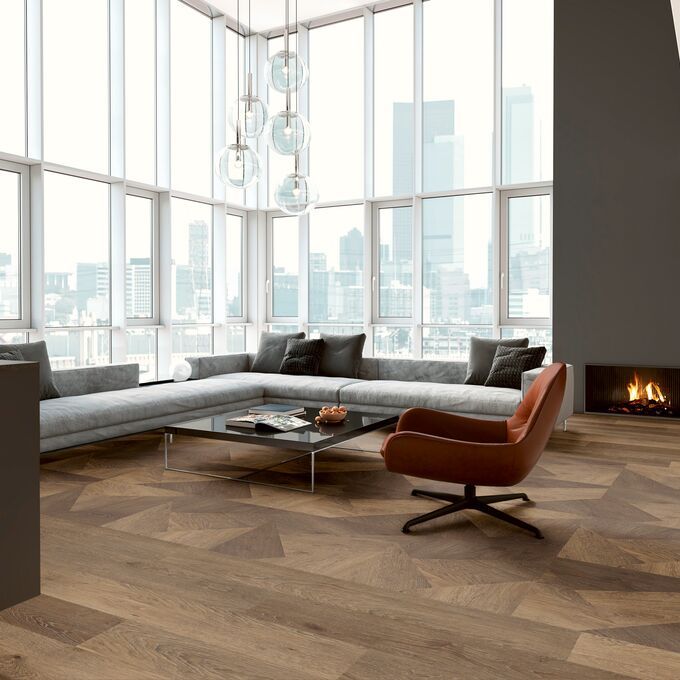 Mixed style oak effect flooring in an apartment with floor to ceiling windows and a large grey couch