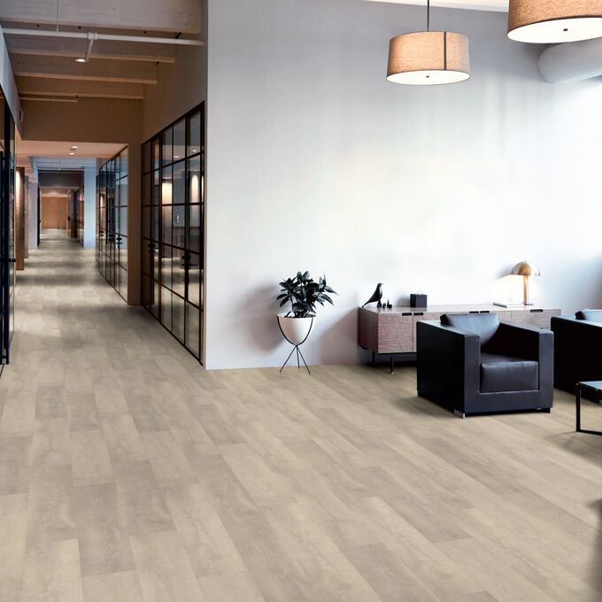 Oak effect flooring in a long corridor with a seating area and black leather chairs
